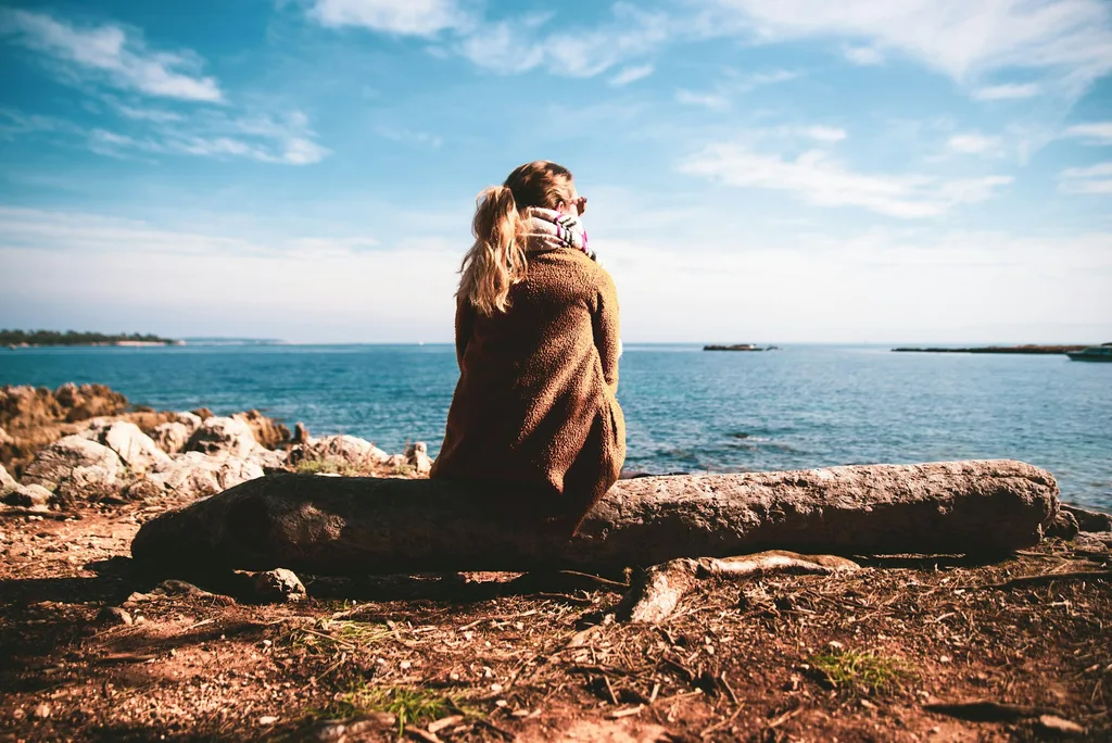A woman sitting quietly outdoors, looking toward the horizon.